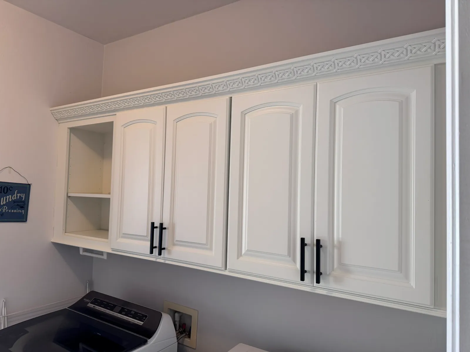 The same laundry room after Valley Painting Pros refinished the cabinets white with black hardware.
