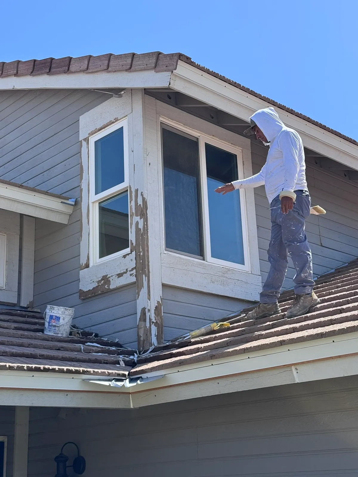 A Valley Painting Pros crew member scraping sun-blistered, peeling paint from a home's exterior before repainting.