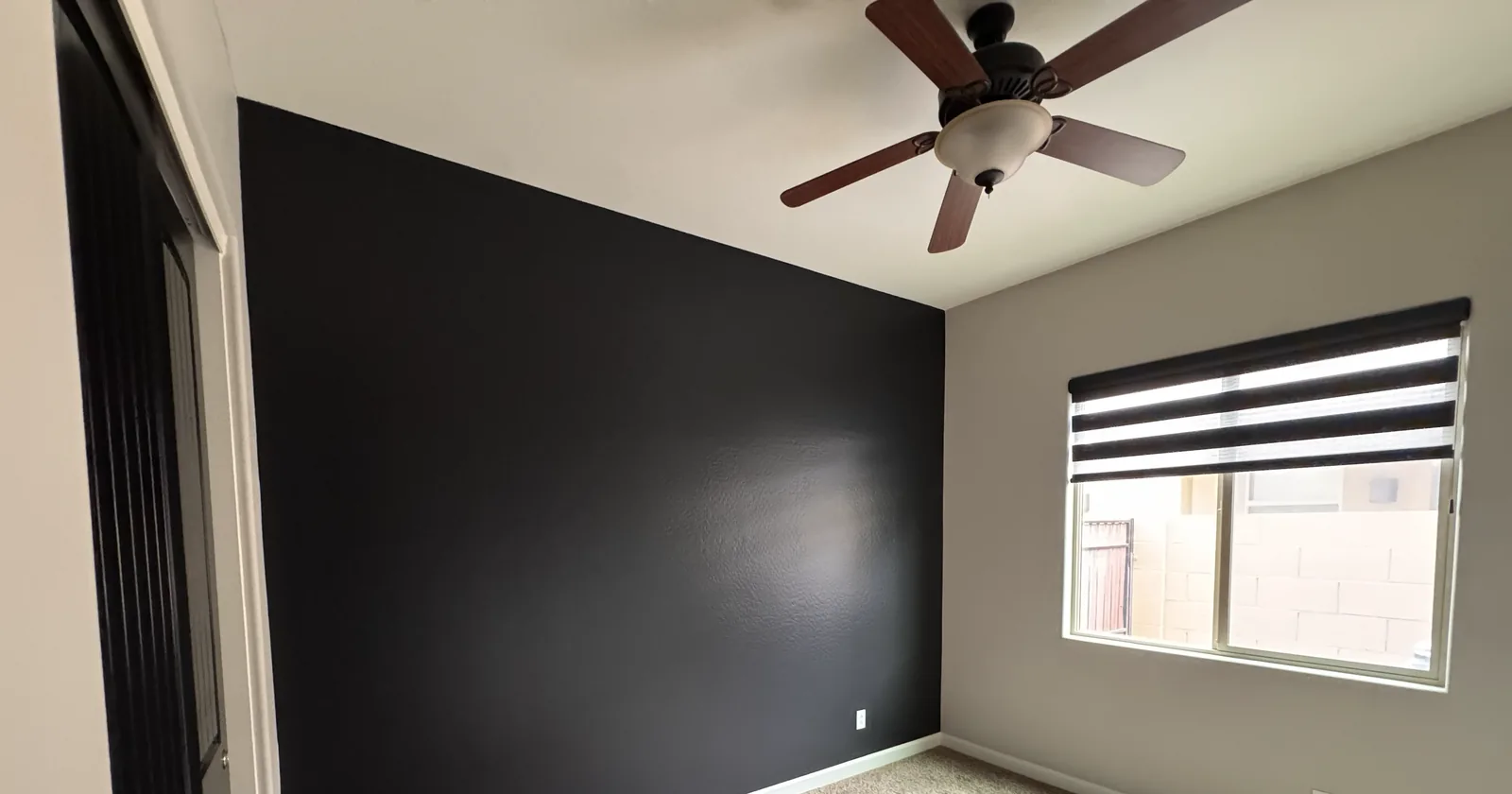 A bedroom with a bold charcoal accent wall and soft gray walls, freshly painted by Valley Painting Pros.