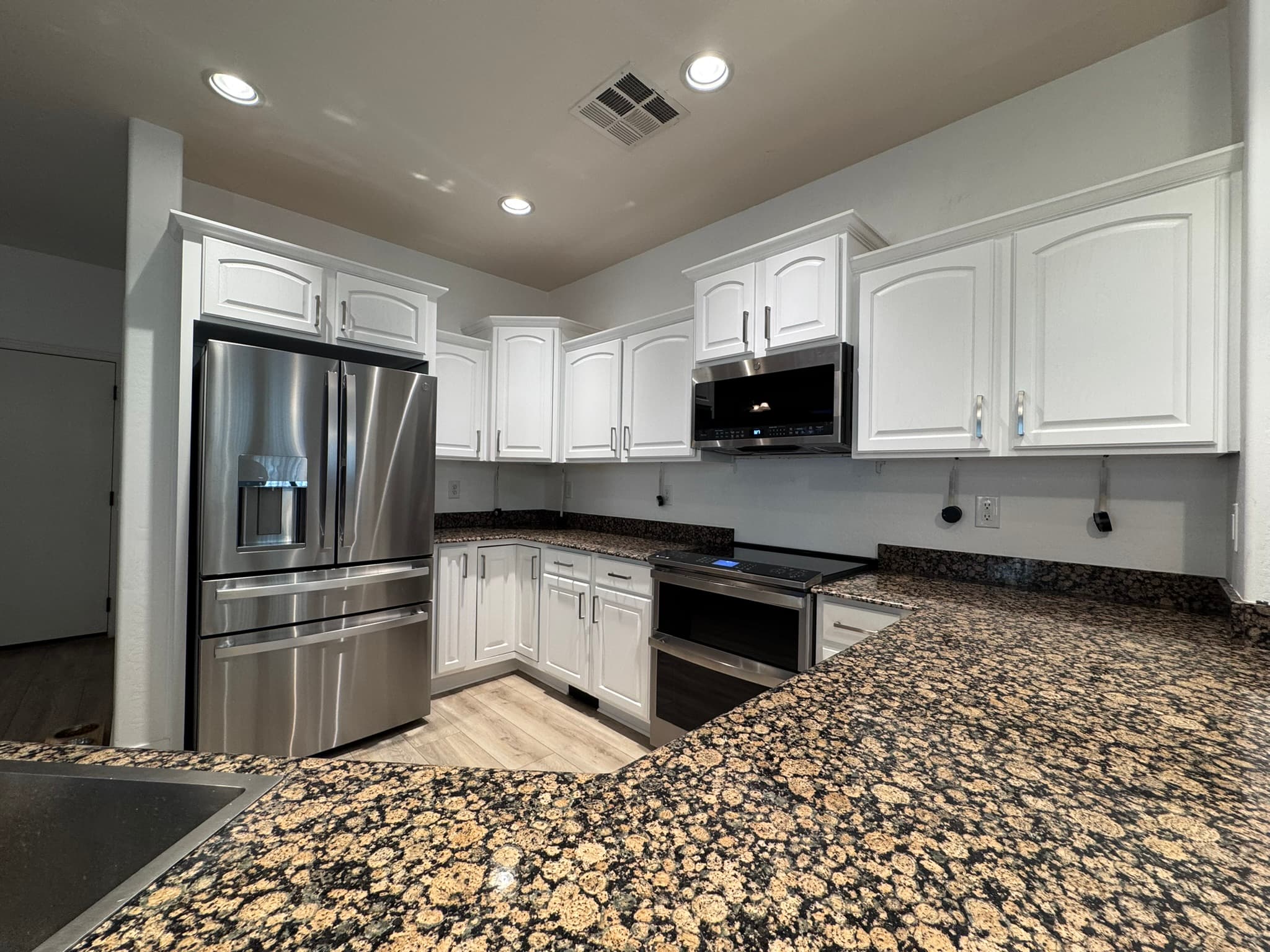 Wide kitchen with refinished white cabinets and granite countertops by Valley Painting Pros